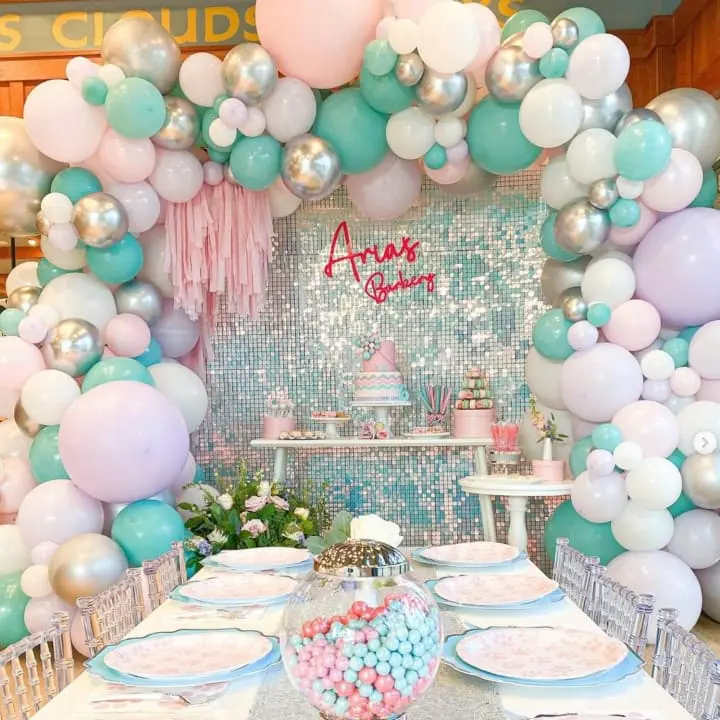 a table set up for a baby shower with balloons and streamers on the wall and plates on the table