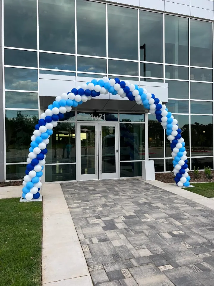 a blue and white balloon arch in front of a large glass building with a brick walkway in front of it