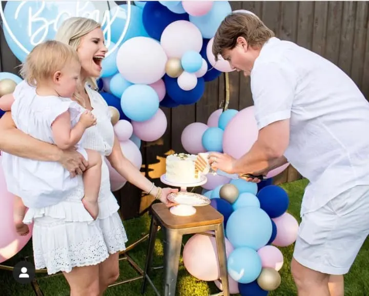 a man and a woman cutting a cake with a baby in front of a bunch of balloons on a table