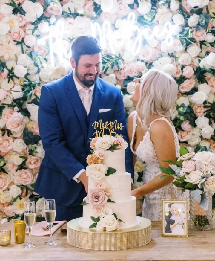 a bride and groom cutting a wedding cake together at a reception table with a floral wall behind them and a floral backdrop behind them