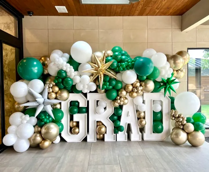 a large balloon arch with the word grand written in white and gold balloons and a star on top of it