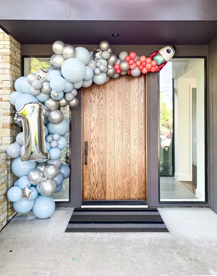 a large balloon arch is decorated with a rocket ship and a bunch of balloons on the front door of a house