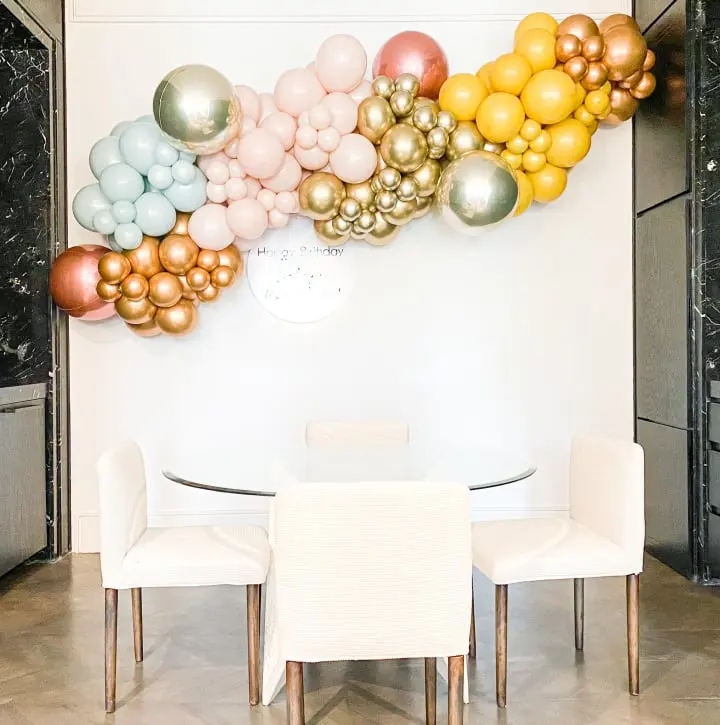a dining room table with a bunch of balloons on the wall above it and a white table and chairs in front of it