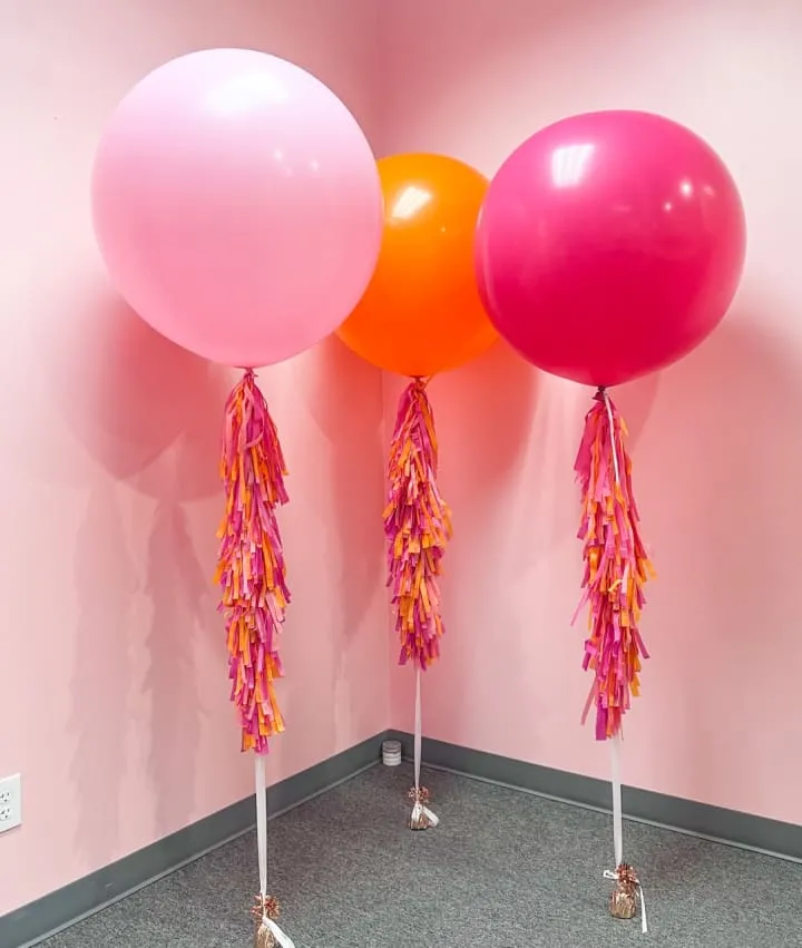three balloons with tassels on them in a room with a pink wall and a pink wall behind them