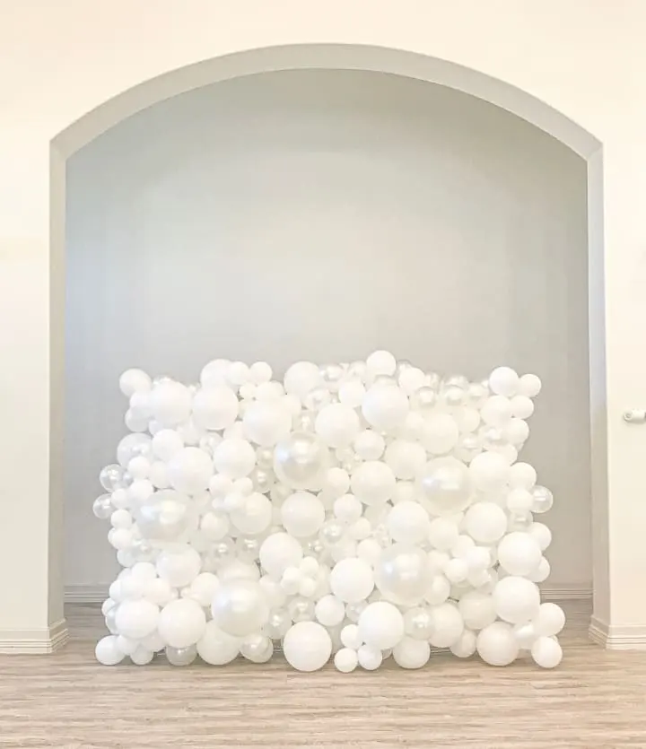 a large white balloon sculpture in a room with a wooden floor and a white wall with a archway in the background