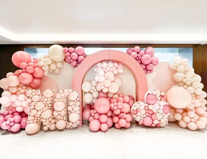 a large number made out of balloons in a room with a white floor and a wall behind it that has a large number made out of balloons in the shape of pink and white letters