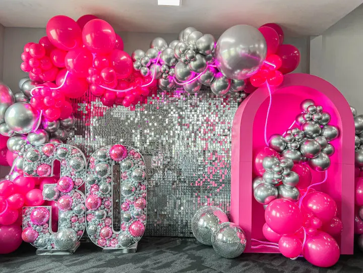 a room with balloons, balloons and a number 50 sign in the center of the room is a wall of silver and pink balloons