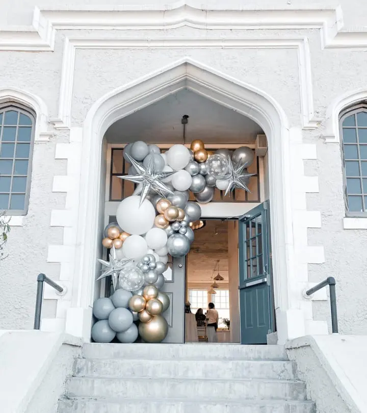 a white building with a bunch of balloons on the front door and a bunch of silver and gold balloons on the front of the door