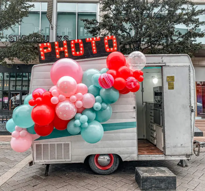a photo booth with balloons and a sign that says photo booth on the side of the truck in front of a building