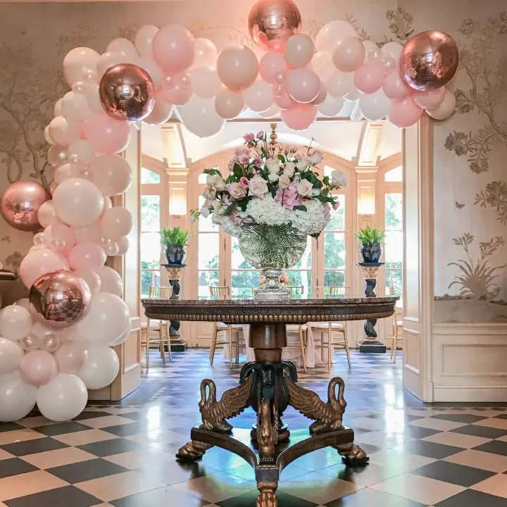 a table with balloons and a vase of flowers on it in a room with a checkerboard floor