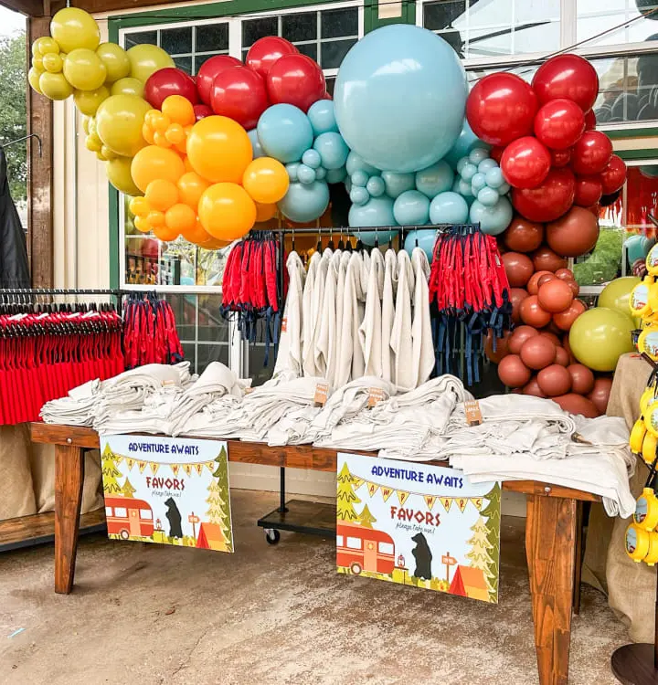 A vibrant and colorful display of balloons, clothing, and other merchandise arranged in an eye-catching manner in front of a building.