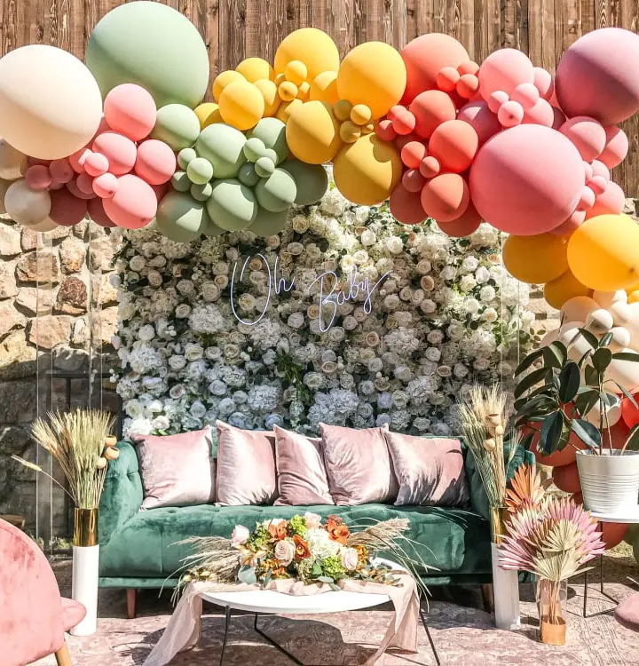 A vibrant and whimsical outdoor setting featuring a cozy seating area surrounded by a colorful array of balloons and lush greenery, creating a festive and inviting atmosphere.
