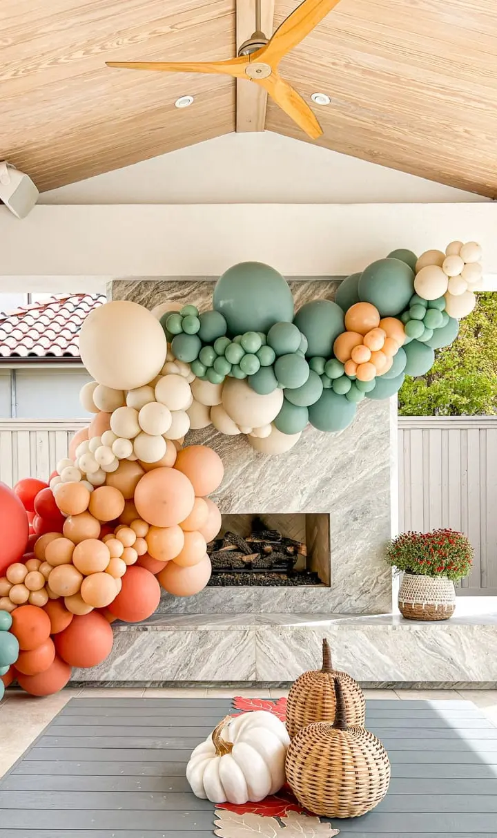 A vibrant and whimsical balloon arch in shades of green, orange, and white adorns the interior of a cozy, rustic-style room, complemented by a fireplace and various decorative elements.